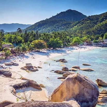 A rocky beach with large boulders, turquoise water and a wooded hill behind